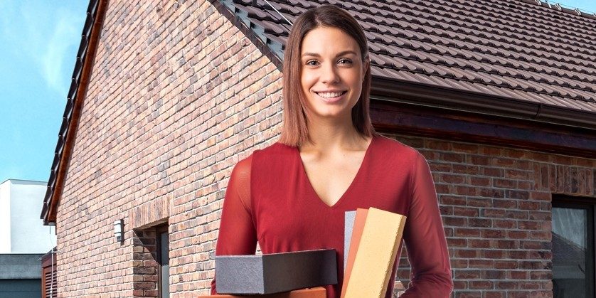 Žena v červených šatech drží klinker obkladové pásky, v pozadí dům s lícovými cihlami