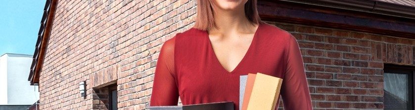 Žena v červených šatech drží klinker obkladové pásky, v pozadí dům s lícovými cihlami